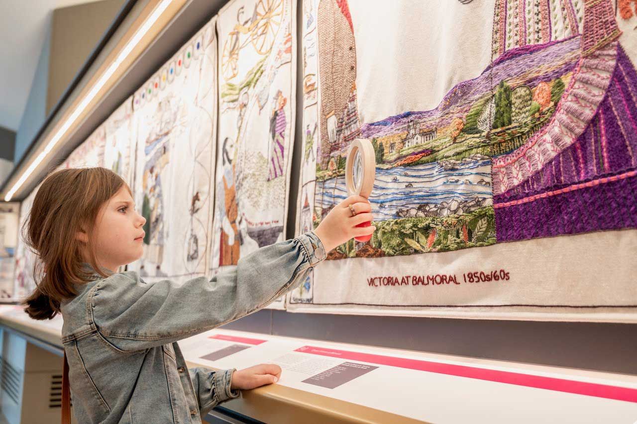 a young girl looking closely at the tapestry with a magnifying glass